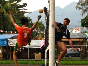 Ilustrasi dua pemain sepak takraw melompat berebut bola di dekat tiang net di Visayas State University, Filipina