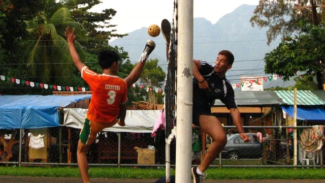 Ilustrasi dua pemain sepak takraw melompat berebut bola di dekat tiang net di Visayas State University, Filipina