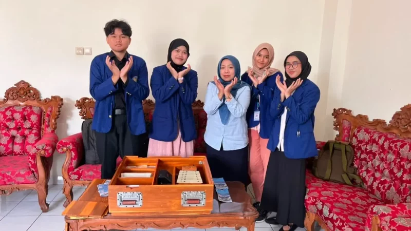 Lima orang berdiri di belakang meja kayu berisi dua kotak media pembelajaran sambil menyilangkan kedua tangan di depan dada.