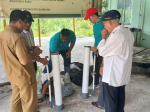 Sejumlah pria berdiri mengelilingi tiga tabung filtrasi putih di halaman berlatar spanduk kegiatan.