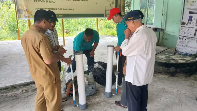Sejumlah pria berdiri mengelilingi tiga tabung filtrasi putih di halaman berlatar spanduk kegiatan.