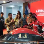 Sejumlah orang mengelilingi mobil hemat energi berwarna hitam dan merah di dalam ruangan berlatar layar bertuliskan Launching.