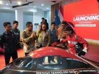 Sejumlah orang mengelilingi mobil hemat energi berwarna hitam dan merah di dalam ruangan berlatar layar bertuliskan Launching.