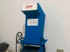 Mesin pencacah plastik berwarna biru dengan corong pemasukan di bagian atas berdiri di dalam ruangan.