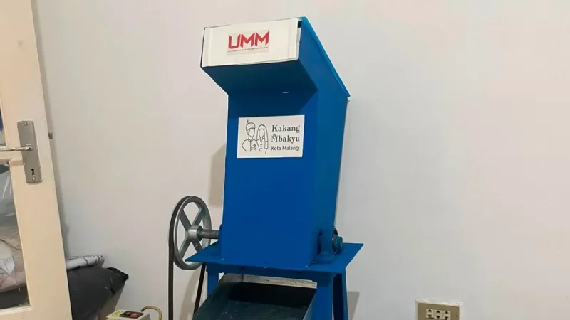 Mesin pencacah plastik berwarna biru dengan corong pemasukan di bagian atas berdiri di dalam ruangan.