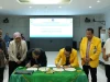 Dua rektor menandatangani dokumen di meja beralas kain hijau disaksikan enam pejabat di ruang rapat berlayar proyektor.