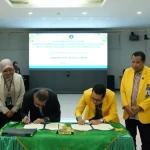 Dua rektor menandatangani dokumen di meja beralas kain hijau disaksikan enam pejabat di ruang rapat berlayar proyektor.