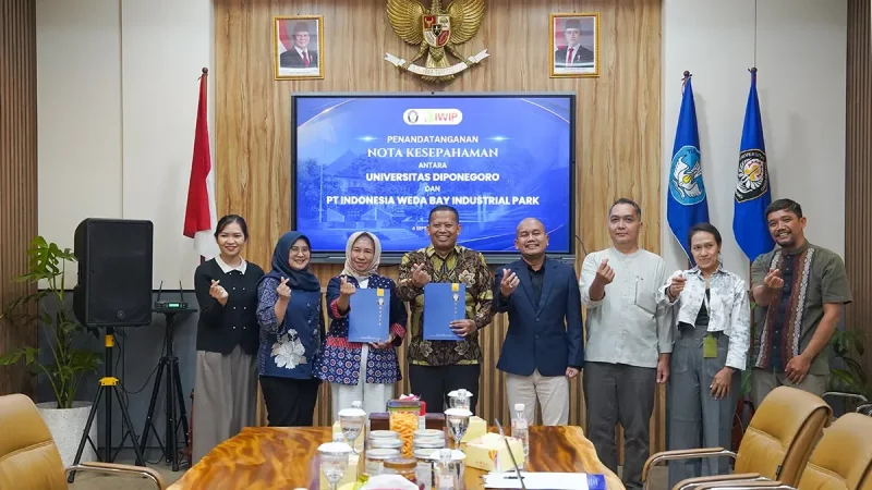 Sembilan orang berdiri berjajar memegang map biru di depan layar bertuliskan penandatanganan nota kesepahaman.