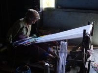 Seorang perempuan menenun hiou, kain tradisional Simalungun, pada alat tenun kayu.