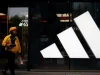 Seorang kurir berjalan melewati gerai Adidas di sebuah pusat perbelanjaan di Beijing, China.
