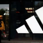 Seorang kurir berjalan melewati gerai Adidas di sebuah pusat perbelanjaan di Beijing, China.