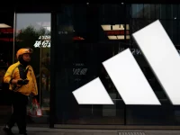 Seorang kurir berjalan melewati gerai Adidas di sebuah pusat perbelanjaan di Beijing, China.