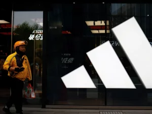 Seorang kurir berjalan melewati gerai Adidas di sebuah pusat perbelanjaan di Beijing, China.
