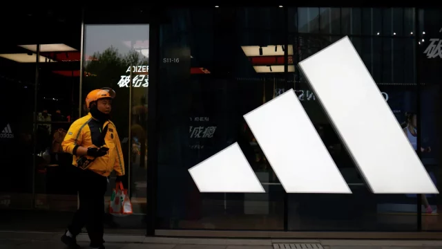 Seorang kurir berjalan melewati gerai Adidas di sebuah pusat perbelanjaan di Beijing, China.