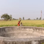 Ilustrasi sebuah sumur terbuka bertembok beton di tepi ladang hijau