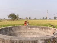 Ilustrasi sebuah sumur terbuka bertembok beton di tepi ladang hijau