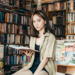 Ilustrasi seorang remaja perempuan membaca buku di antara rak toko buku.