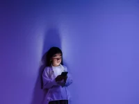 Seorang anak menatap layar ponsel yang menyala di ruangan berpencahayaan biru