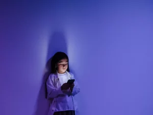 Seorang anak menatap layar ponsel yang menyala di ruangan berpencahayaan biru