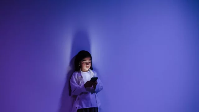 Seorang anak menatap layar ponsel yang menyala di ruangan berpencahayaan biru