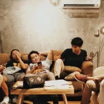 Enam anak muda duduk bersantai di sofa kafe sambil memegang ponsel