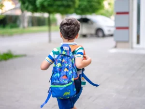 Ilustrasi anak berjalan mengenakan tas ransel ke sekolah.
