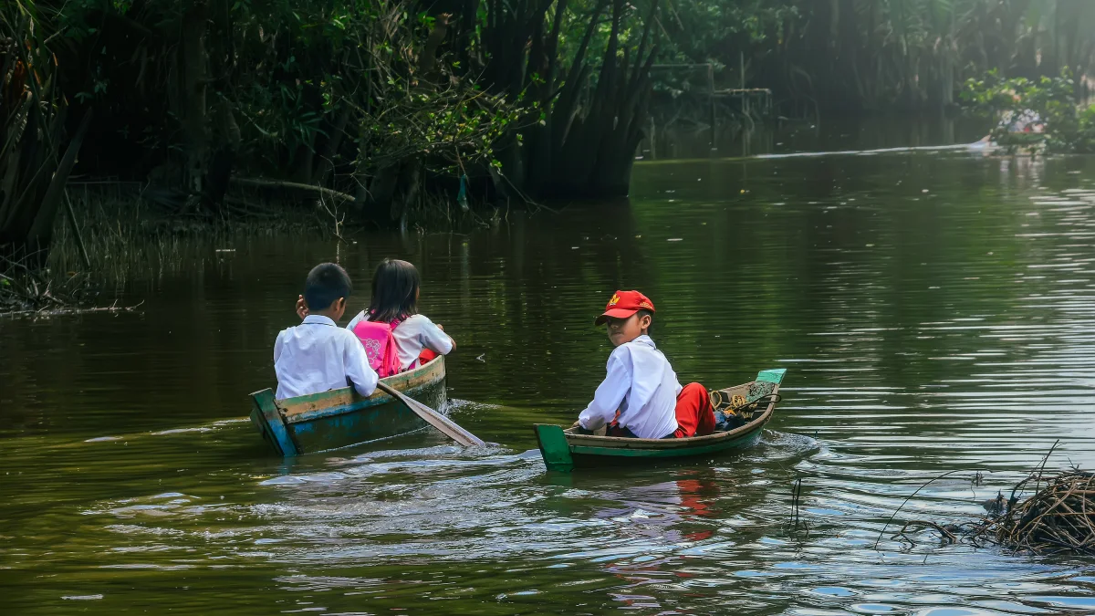 Anak-anak berseragam sekolah berangkat menyeberangi sungai dengan perahu kayu