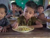 Anak-anak sekolah dasar makan siang nasi dan sayur di meja kayu ruang kelas