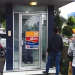 Beberapa orang berdiri di depan bilik ATM sebuah bank di tepi jalan