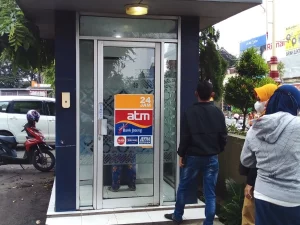 Beberapa orang berdiri di depan bilik ATM sebuah bank di tepi jalan