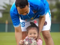 Ayah berkaus bola biru mendampingi putri kecilnya yang memegang bola di lapangan rumput, Jakarta