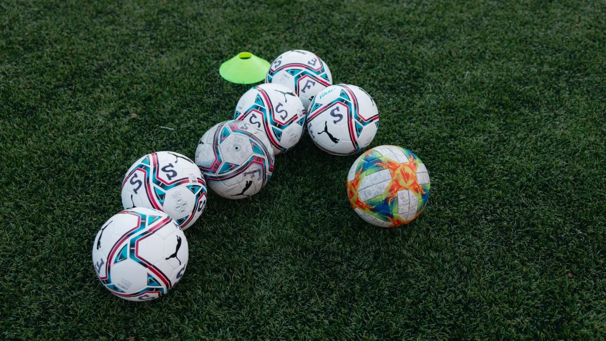 Delapan bola sepak dan satu kerucut latihan kuning di atas lapangan rumput