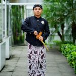 Ilustrasi seorang lelaki berbusana tradisi Jawa berdiri di halaman berpepohonan.