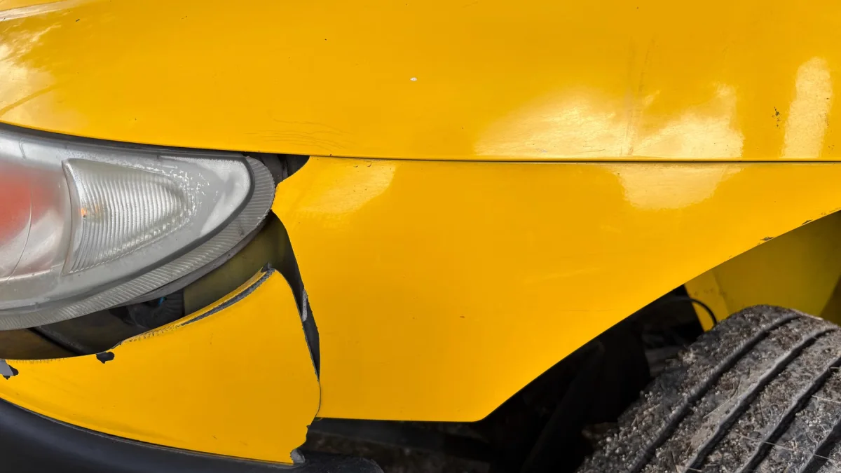 Bumper depan mobil kuning penyok di dekat lampu depan dan roda