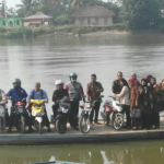 Perahu ketek penuh penumpang dan sepeda motor menyeberangi Sungai Komering.