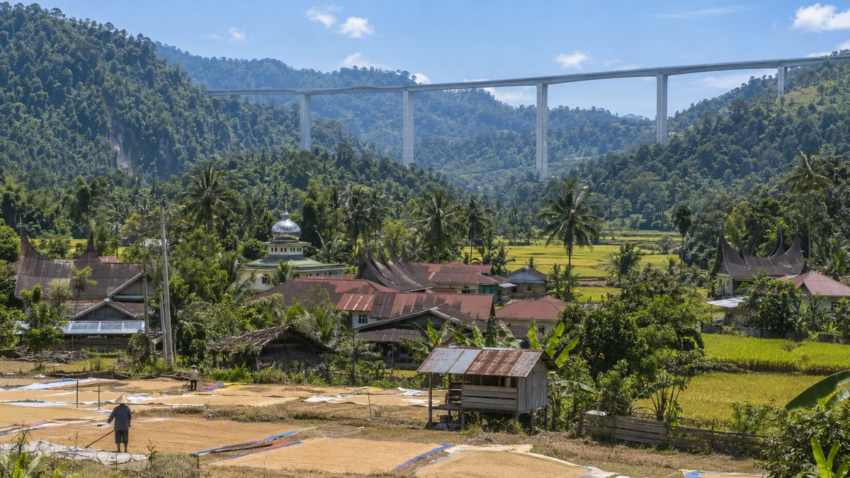 Nagari dengan rumah gonjong dan hamparan gabah dilalui jalan tol layang di kejauhan