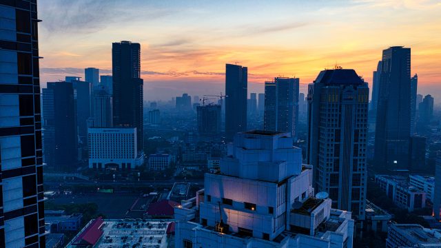 Ilustrasi gedung-gedung bertingkat di kawasan pusat kota menjelang malam.