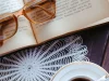 Ilustrasi buku terbuka dengan kacamata baca dan secangkir kopi di atas meja
