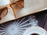 Ilustrasi buku terbuka dengan kacamata baca dan secangkir kopi di atas meja