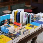 Ilustrasi buku-buku tersusun di atas meja kayu sebuah toko buku.