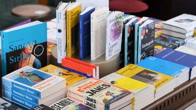 Ilustrasi buku-buku tersusun di atas meja kayu sebuah toko buku.
