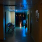 Ilustrasi lorong bangunan berlampu remang dengan deretan kursi tunggu kosong.