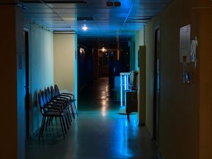 Ilustrasi lorong bangunan berlampu remang dengan deretan kursi tunggu kosong.