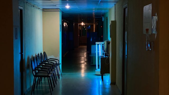 Ilustrasi lorong bangunan berlampu remang dengan deretan kursi tunggu kosong.