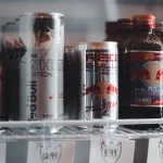 Kaleng dan botol minuman energi berjajar di rak lemari pendingin toko berlabel harga