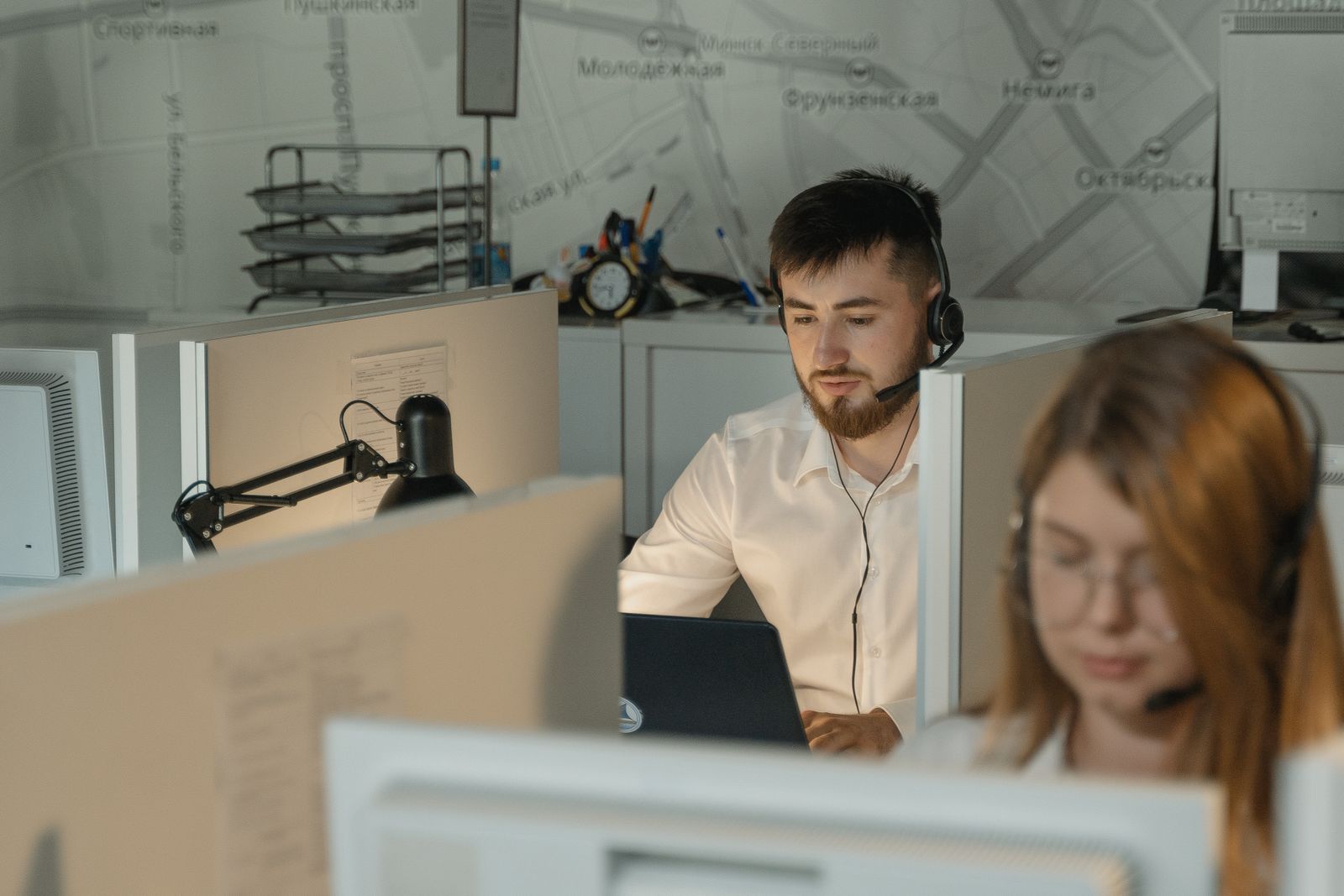 Ilustrasi dua pekerja mengenakan headset duduk berdampingan di depan komputer di sebuah kantor layanan telepon.