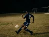 Dua pemain sepak bola berebut bola di lapangan rumput pada malam hari