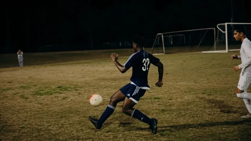 Dua pemain sepak bola berebut bola di lapangan rumput pada malam hari