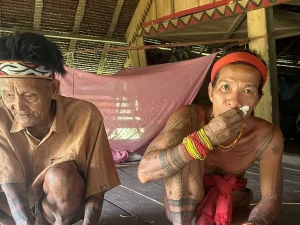 Dua sikerei Mentawai lanjut usia bertato duduk di lantai rumah uma