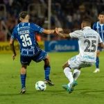 Dua pemain sepak bola berebut bola di lapangan berumput hijau